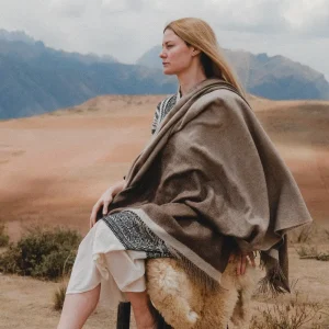 Baby alpaca blanket in brown wrapped around a woman sitting outdoors in peru
