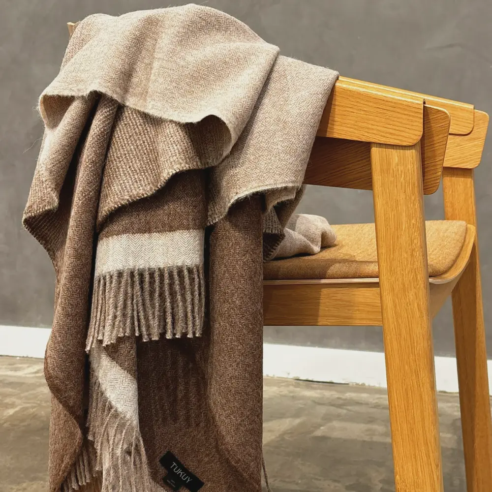 Baby alpaca blanket in brown draped over a wooden chair highlighting its soft texture
