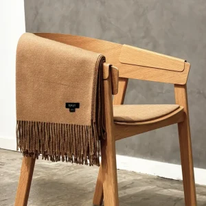 Camel baby alpaca wool blanket folded over a modern wooden chair with soft fringes – sustainable luxury throw made in Peru