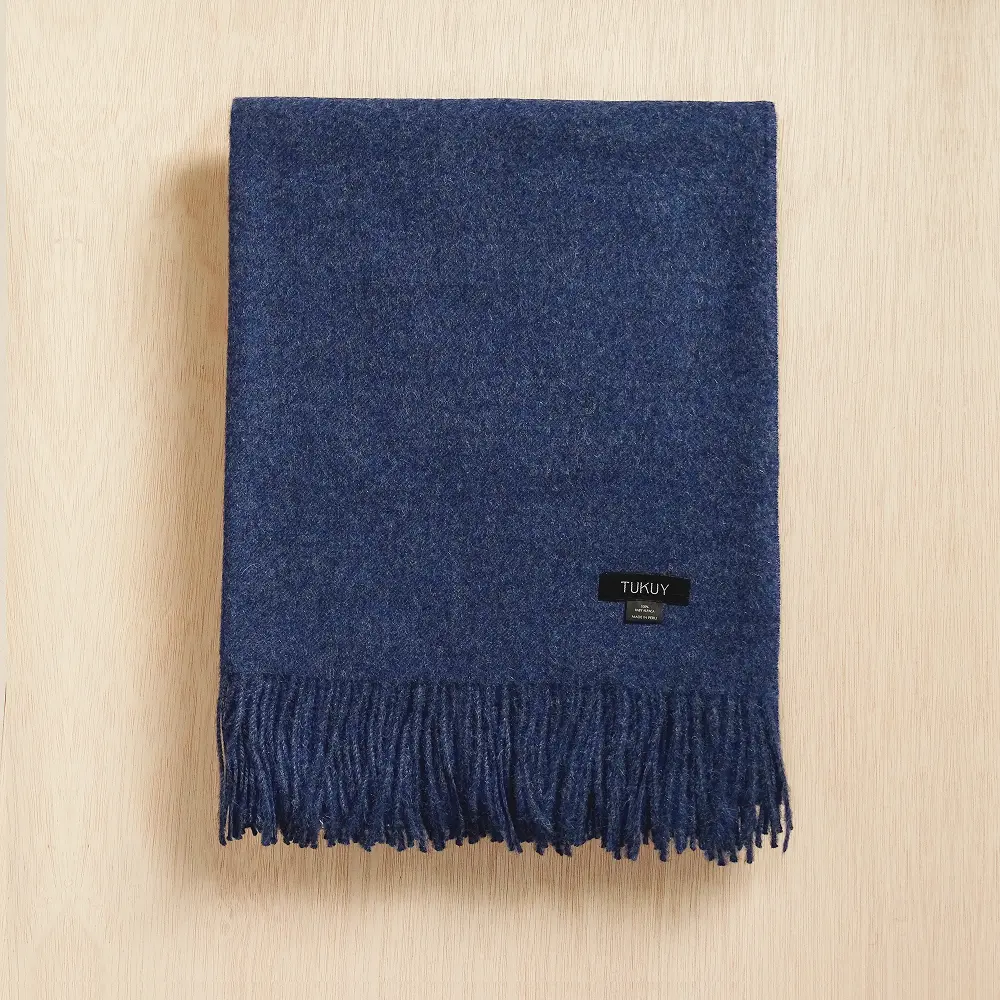 Baby alpaca blanket in deep blue folded on a neutral background with elegant fringe