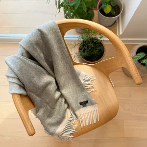 Baby alpaca blanket in grey draped over a wooden chair with elegant fringe