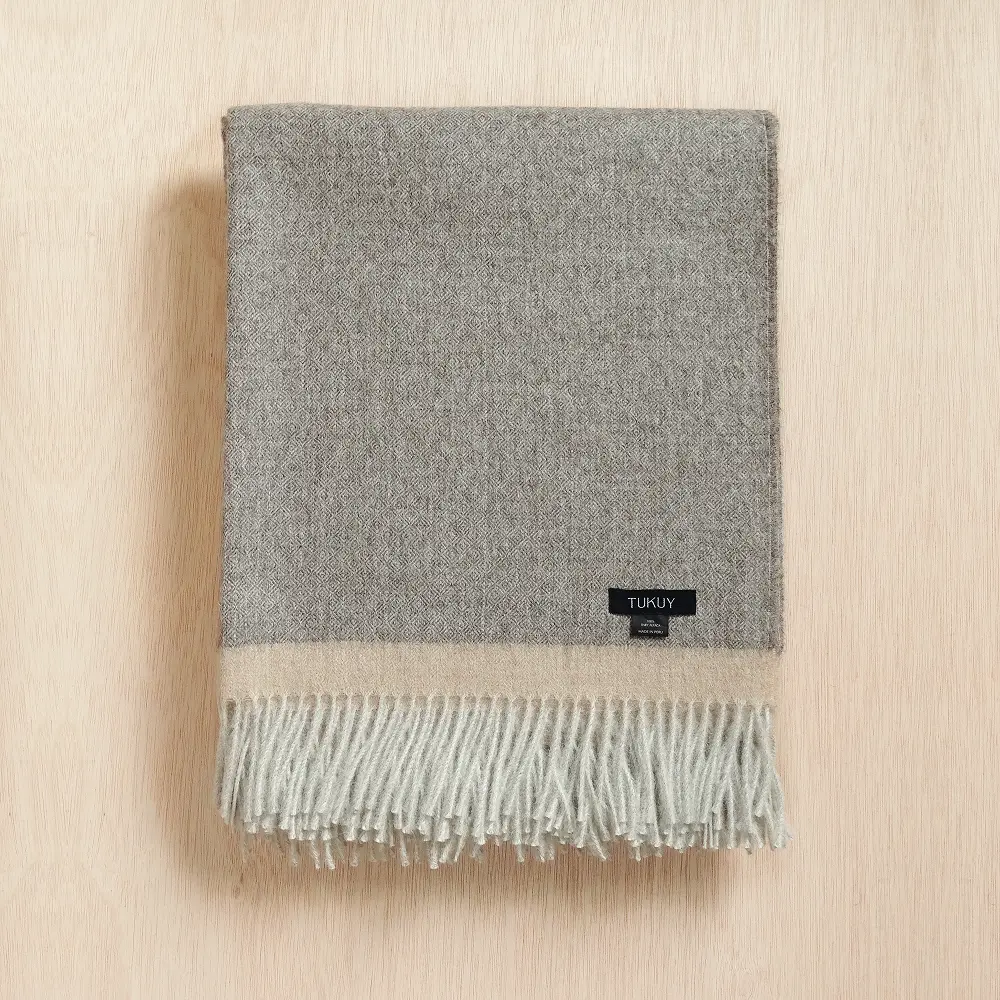 Baby alpaca blanket in grey folded on a neutral background with fringe details