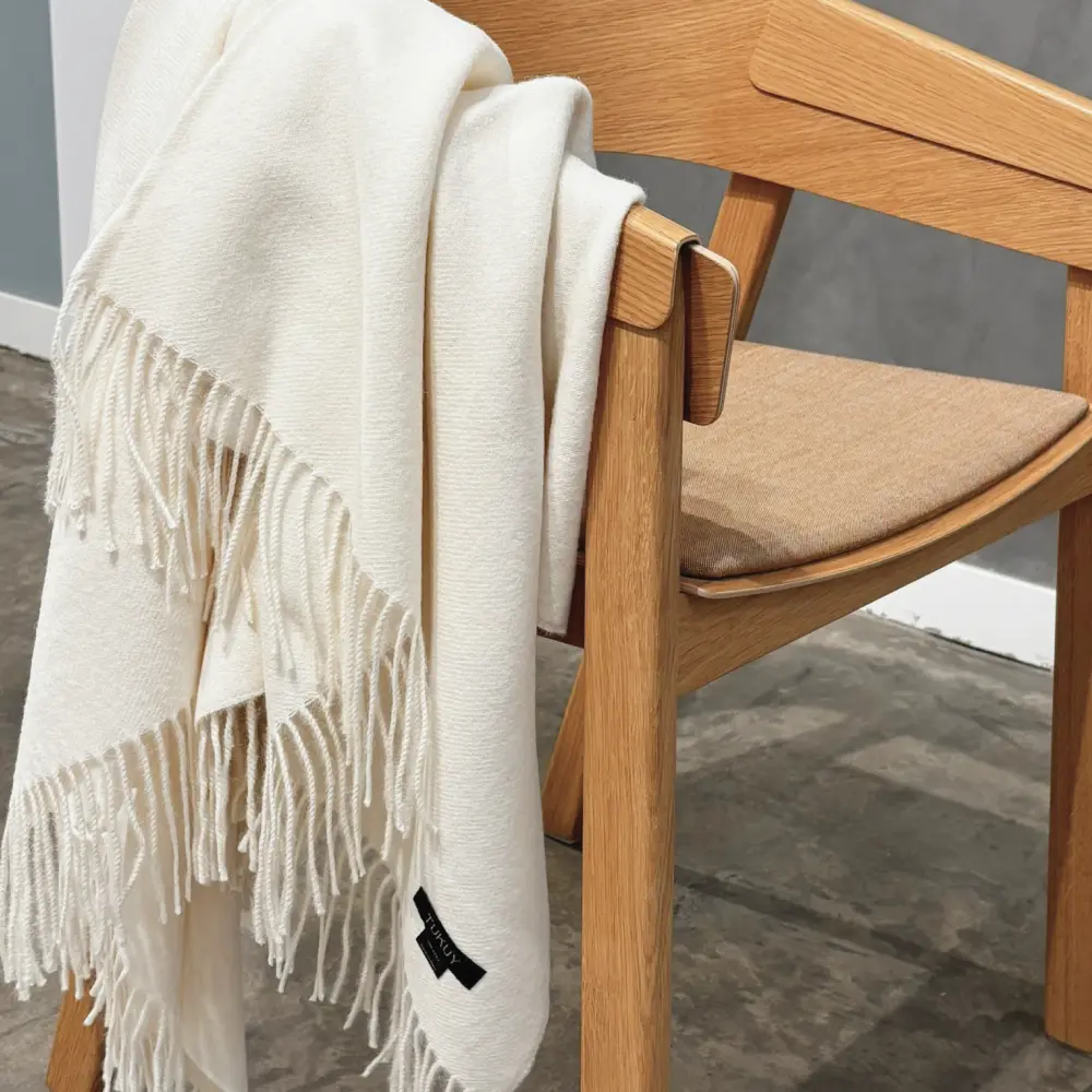 Baby alpaca blanket in white folded over a wooden chair showcasing its luxurious softness