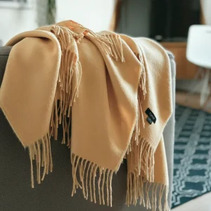 Baby alpaca blanket in pastel mustard yellow draped over a chair showcasing its luxurious softness