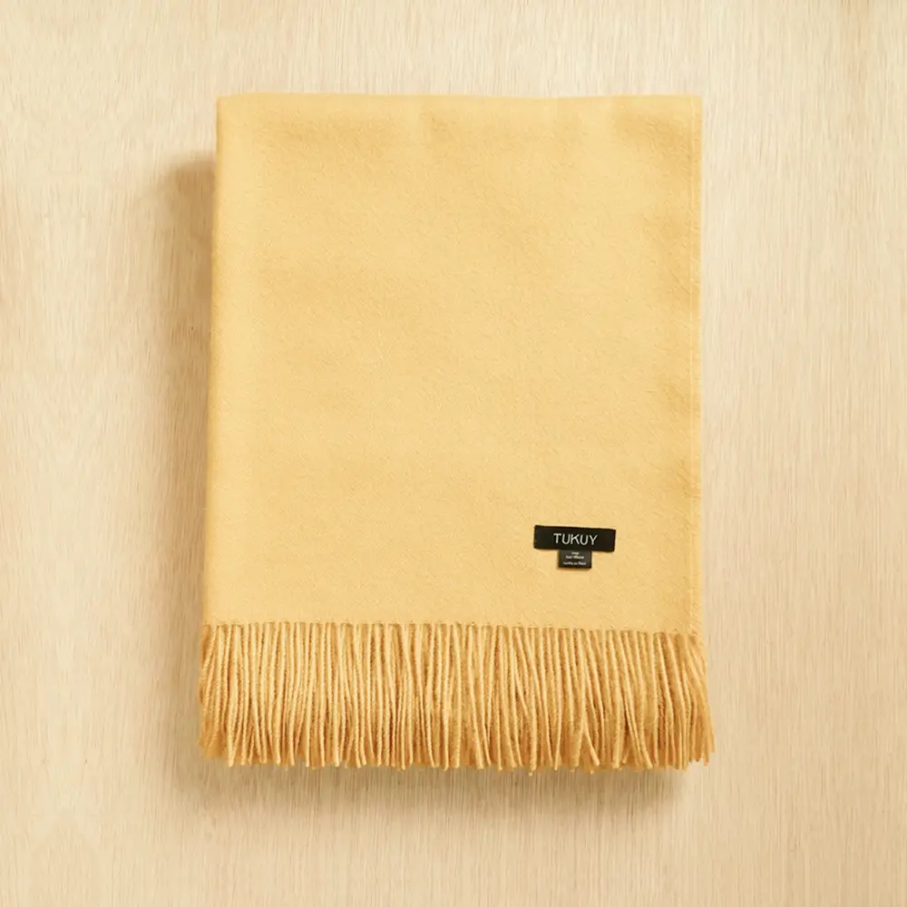 Baby alpaca blanket in pastel mustard yellow folded on a neutral background with fringe details