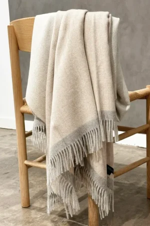 Baby alpaca blanket in beige and light grey styled over a wooden chair in a modern interior