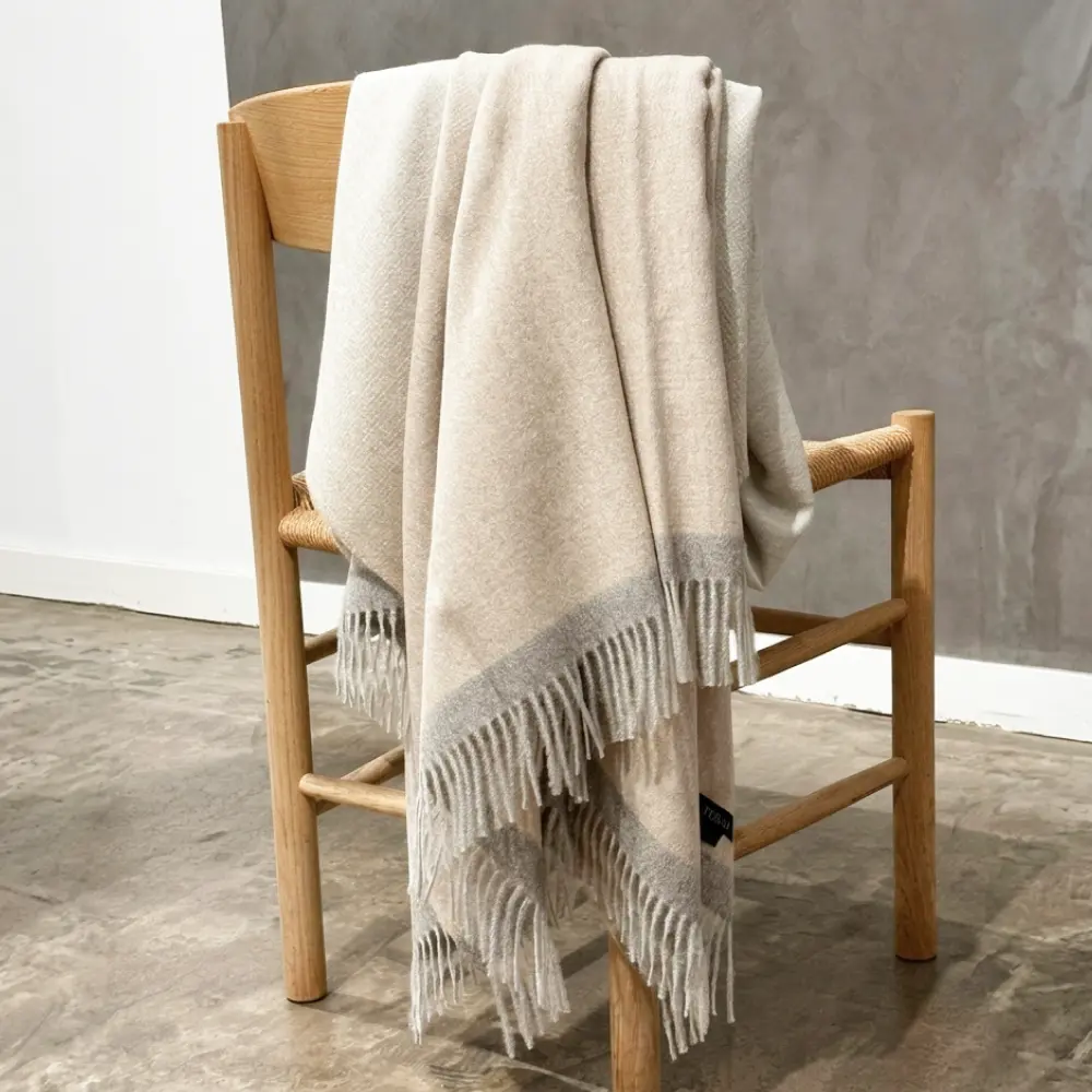 Baby alpaca blanket in beige and light grey styled over a wooden chair in a modern interior