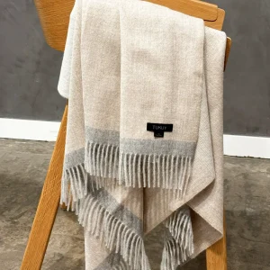 Baby alpaca blanket in beige and light grey draped over a wooden chair showcasing its soft texture