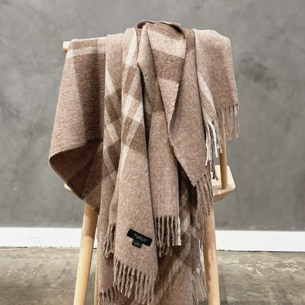 Manta de baby alpaca a cuadros marrones sobre una silla de madera