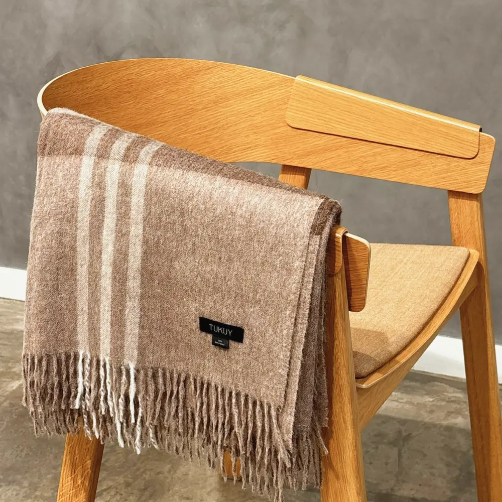 Baby alpaca blanket in brown check folded over a wooden chair with elegant fringe