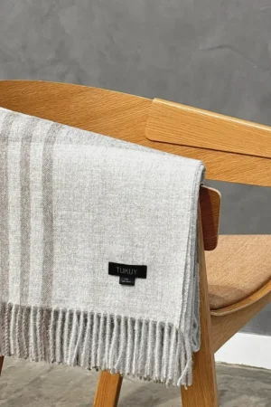 Baby alpaca blanket in light grey check folded over a wooden chair with fringe details