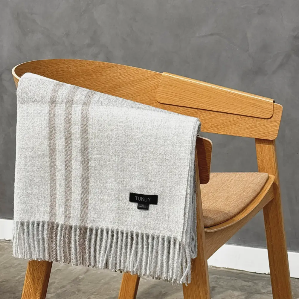 Baby alpaca blanket in light grey check folded over a wooden chair with fringe details