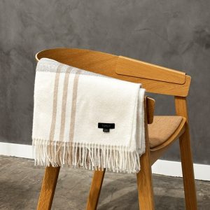 baby alpaca plaid blanket folded over a wooden chair with elegant fringe details sand and stone colored