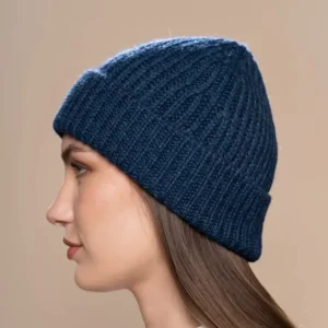 Frau im Profil mit blauer gestrickter Alpaka-Mütze vor neutralem Hintergrund