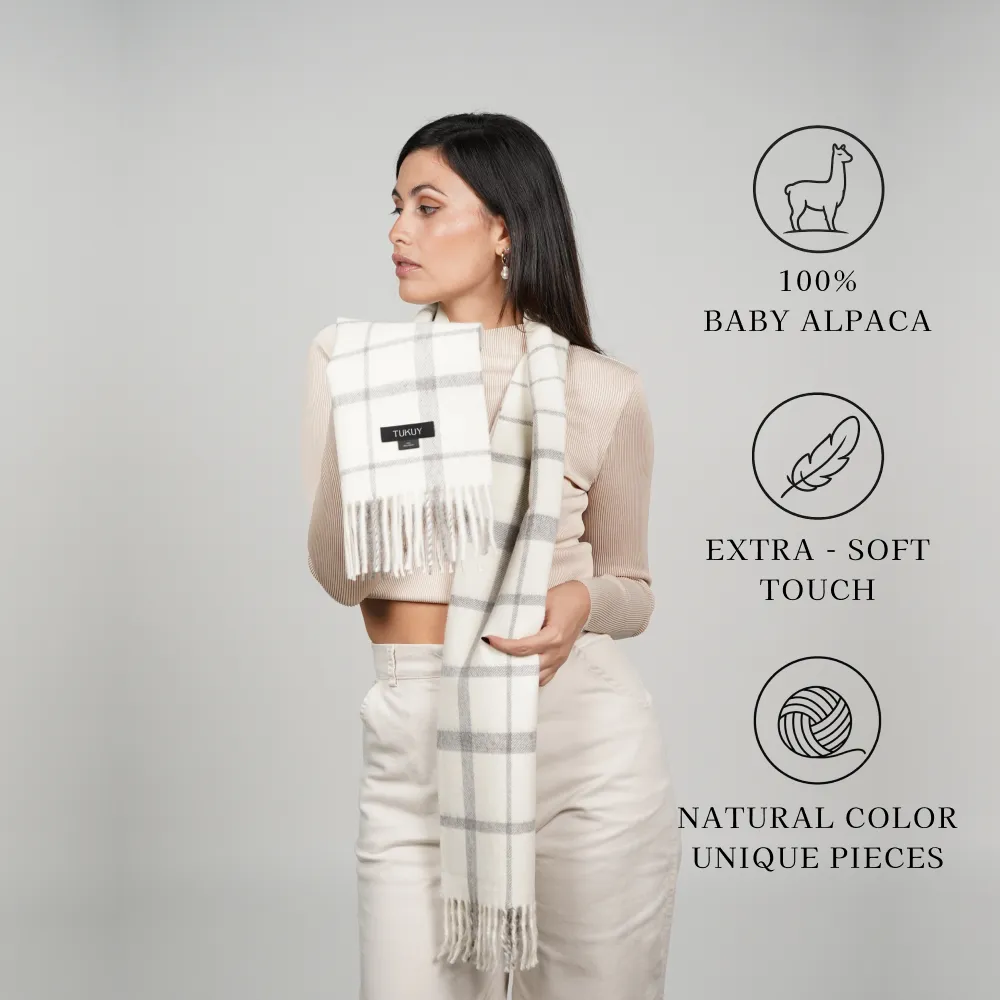 Model wearing a white-and-gray plaid scarf labeled 100% baby alpaca, extra-soft touch, and natural color unique pieces
