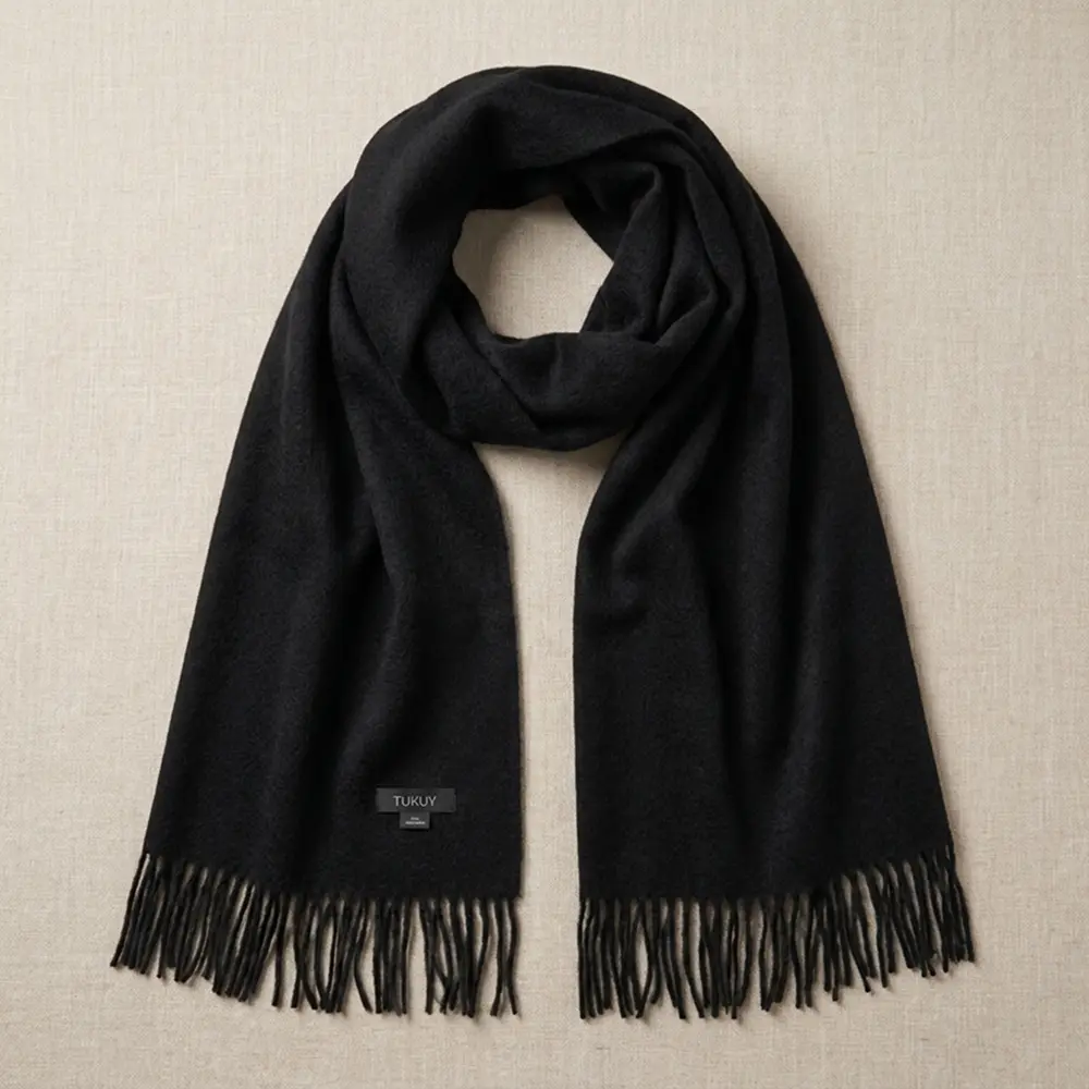 Baby alpaca scarf in black folded on a neutral background with fringe details