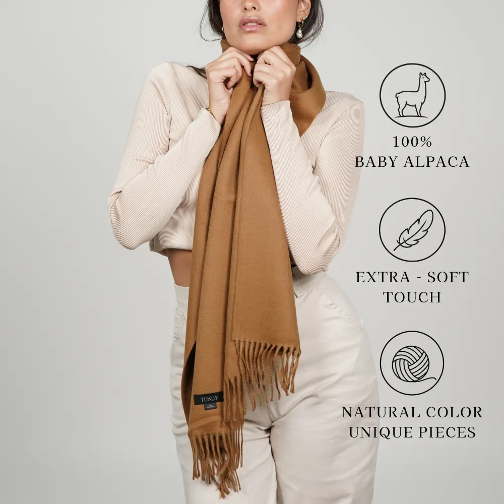 Model wearing a camel scarf labeled 100% baby alpaca, extra-soft touch, natural color, unique pieces