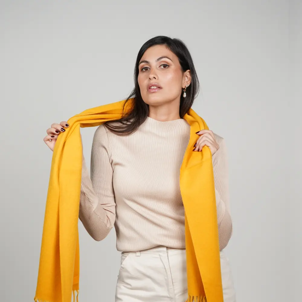 Baby alpaca scarf in mustard yellow worn over the shoulders by a woman