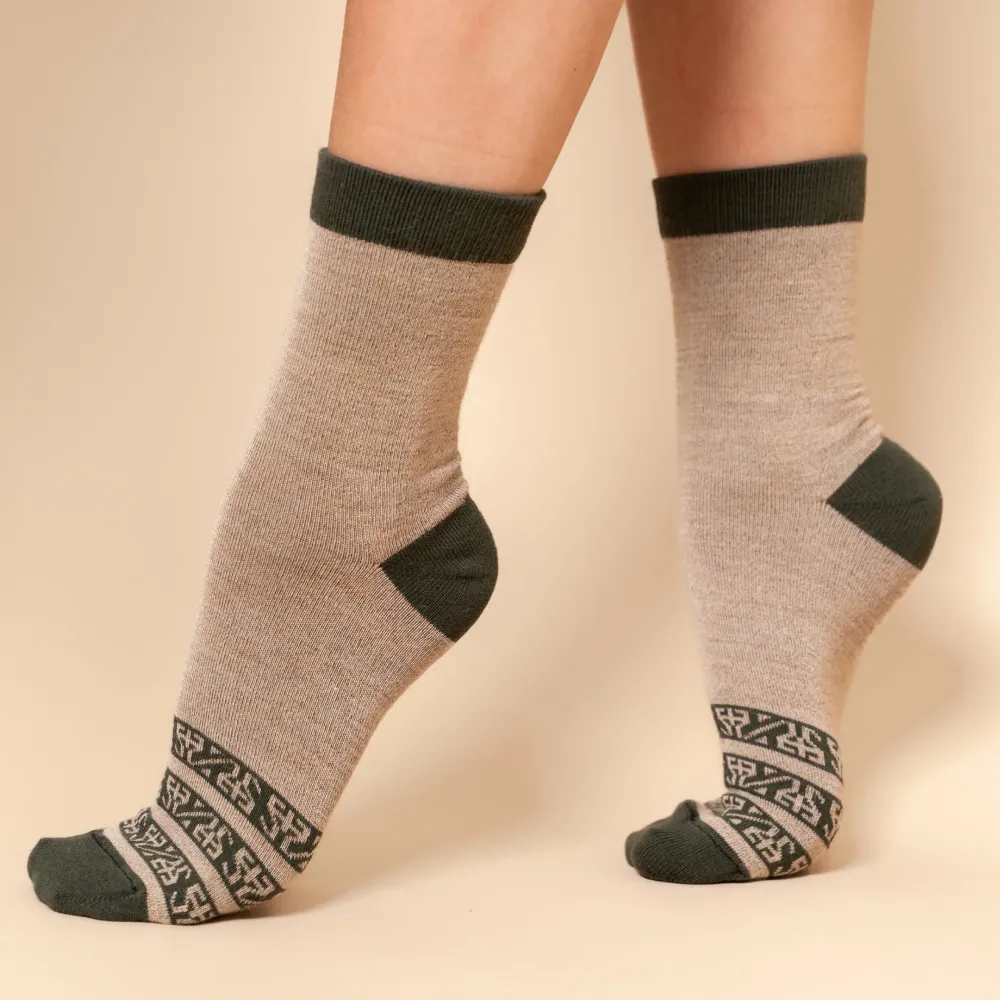 Beige alpaca socks with dark green cuffs, heels, toes, and patterned ankle bands worn on feet