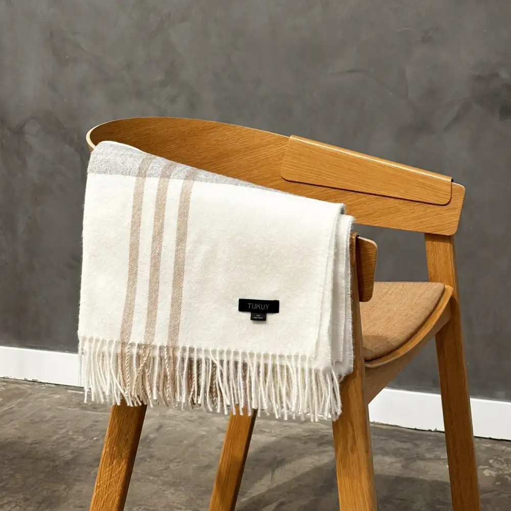 baby alpaca plaid blanket folded over a wooden chair with elegant fringe details sand and stone colored