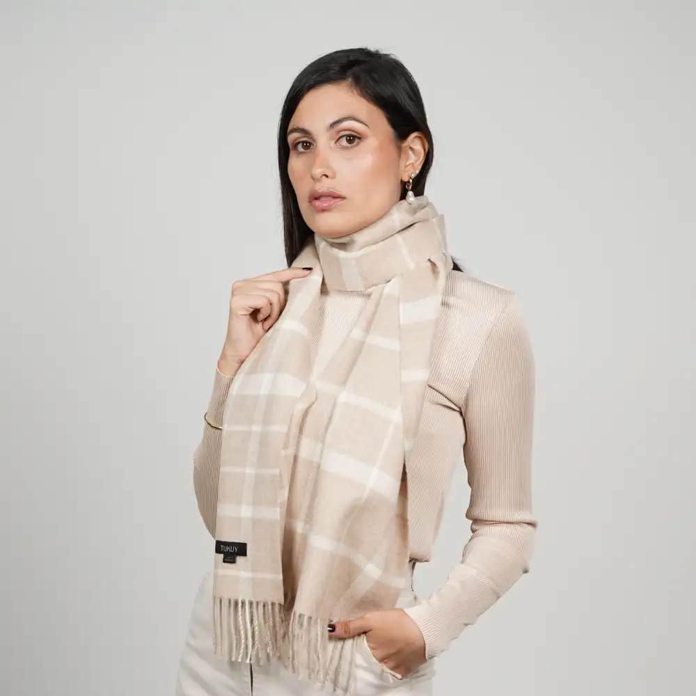 Eine Frau trägt einen beigen Alpaka-Schal mit Karomuster, der sich durch ein zeitloses Fensterkaro-Muster in sanften Beige- und Cremetönen auszeichnet und dessen eleganter Fall sowie sein vielseitiges, neutrales Design zur Geltung kommen.